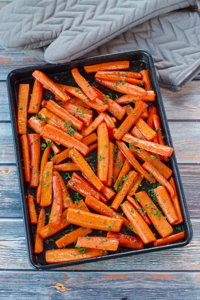 roasted carrots with brown sugar on a black sheet pan on blue faux wood surface