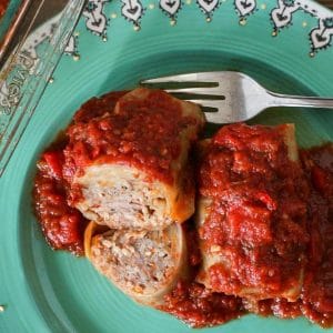 Cabbage rolls with dill and roasted red pepper on a green patterned plate with fork (and 1 cabbage roll cut in half)