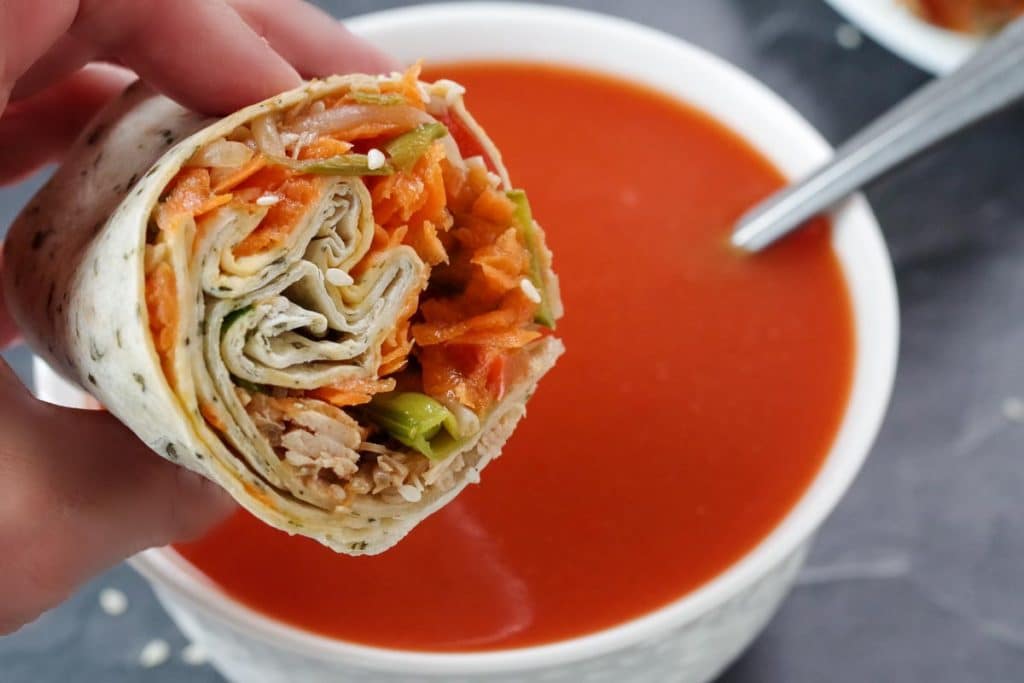half a turkey wrap being held up over a bowl of tomato soup