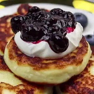 syrniki pancakes stacked with sour cream and blueberry sauce