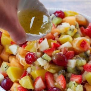 easy fruit salad in white bowl with honey lime dressing being poured over salad