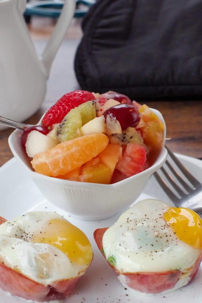 fruit salad in a cup, on a white plate, with healthy eggs benedict