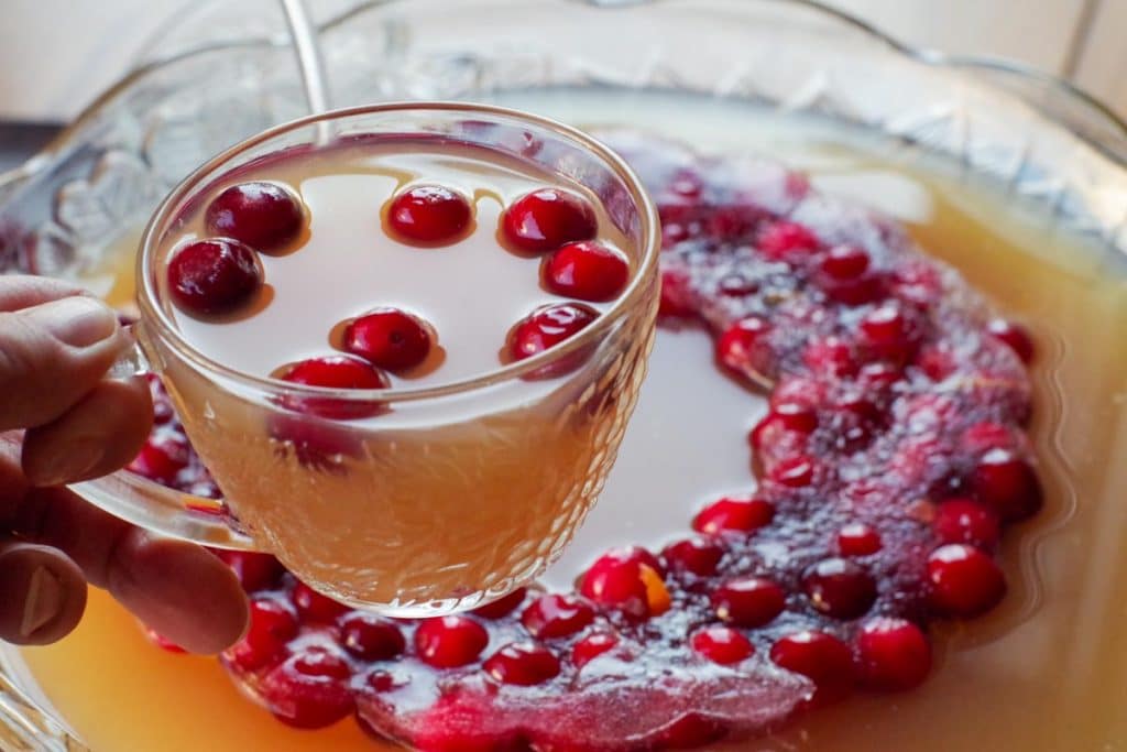 Cranberry Christmas Punch being held up in a glass over a punch bowl with a cranberry punch ring