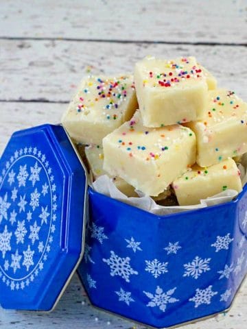 Microwave sugar cookie fudge in blue cookie tin on white faux wood surface
