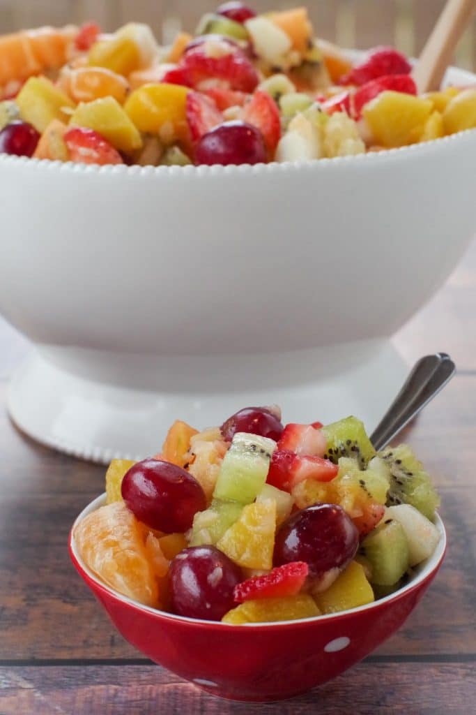 classic fruit salad in a small red bowl with white polkadots and a large white bowl of salad in the background