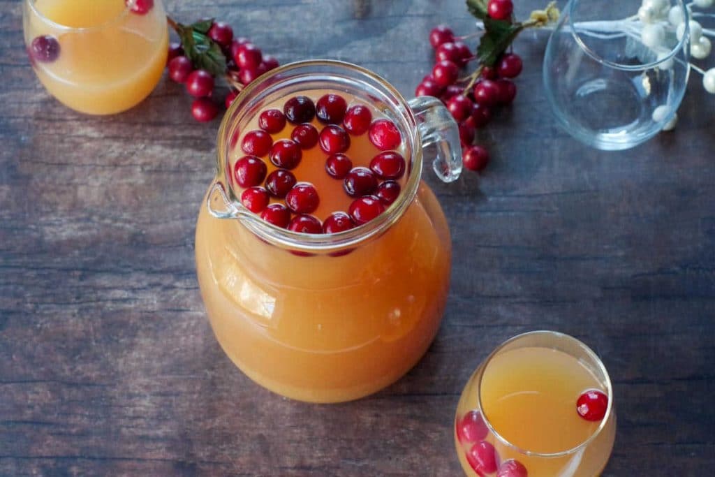cranberry orange punch in a glass pitcher with glasses and cranberries in background