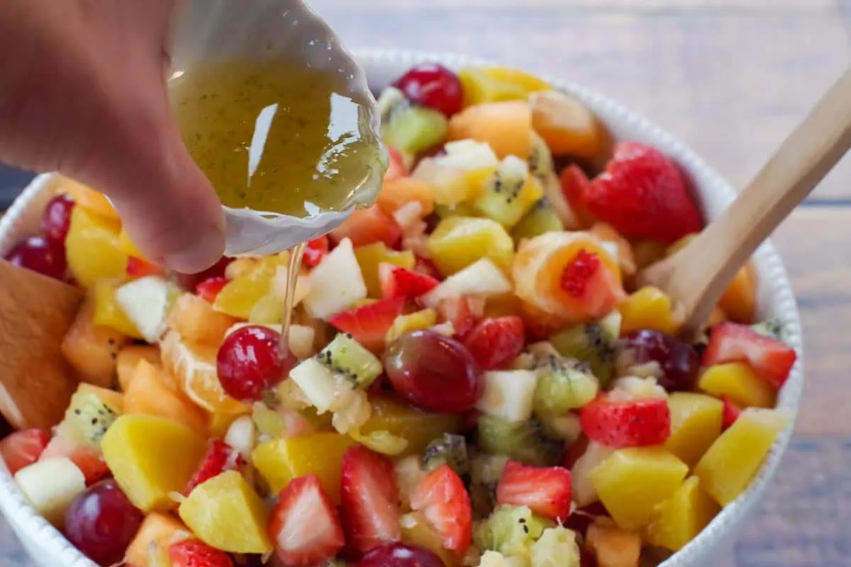 easy fruit salad in white bowl with honey lime dressing being poured over salad