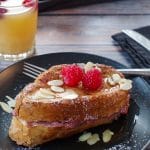French Toast Sandwich on a black plate with fork and glass of juice in background