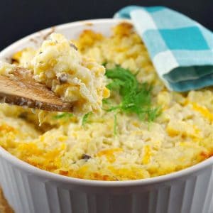 Potatoes Romanoff in a white casserole bowl, being held up with a wooden spoon