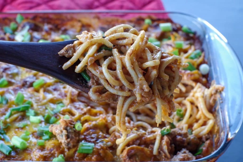 Million Dollar Spaghetti Casserole being held up on a spoon over glass casserole dish