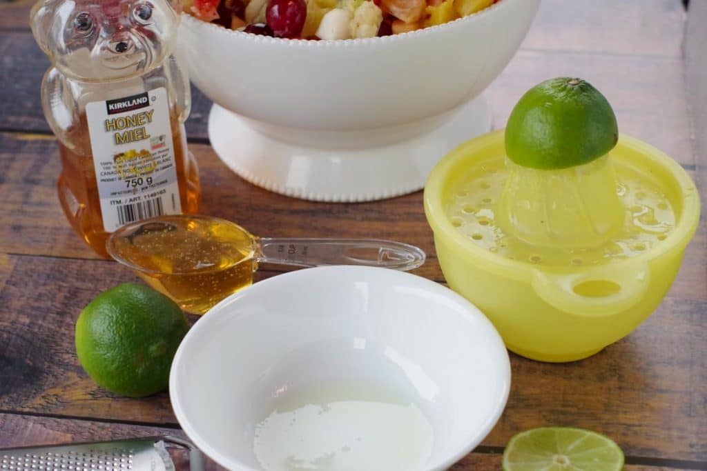 bottle of liquid home, lime, lime being juiced on yellow juicer, with bowl of lime juice in front and zester on the side