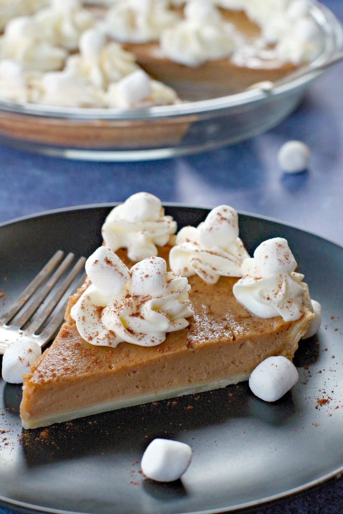 sweet potato pie on black plate on blue background with marshmallows around and pie in background