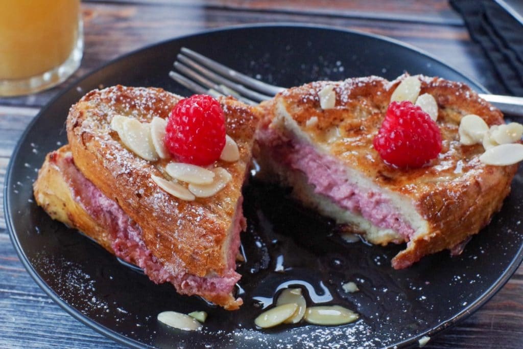 Raspberry French Toast Sandwich cut in half on a black plate, with fork on plate