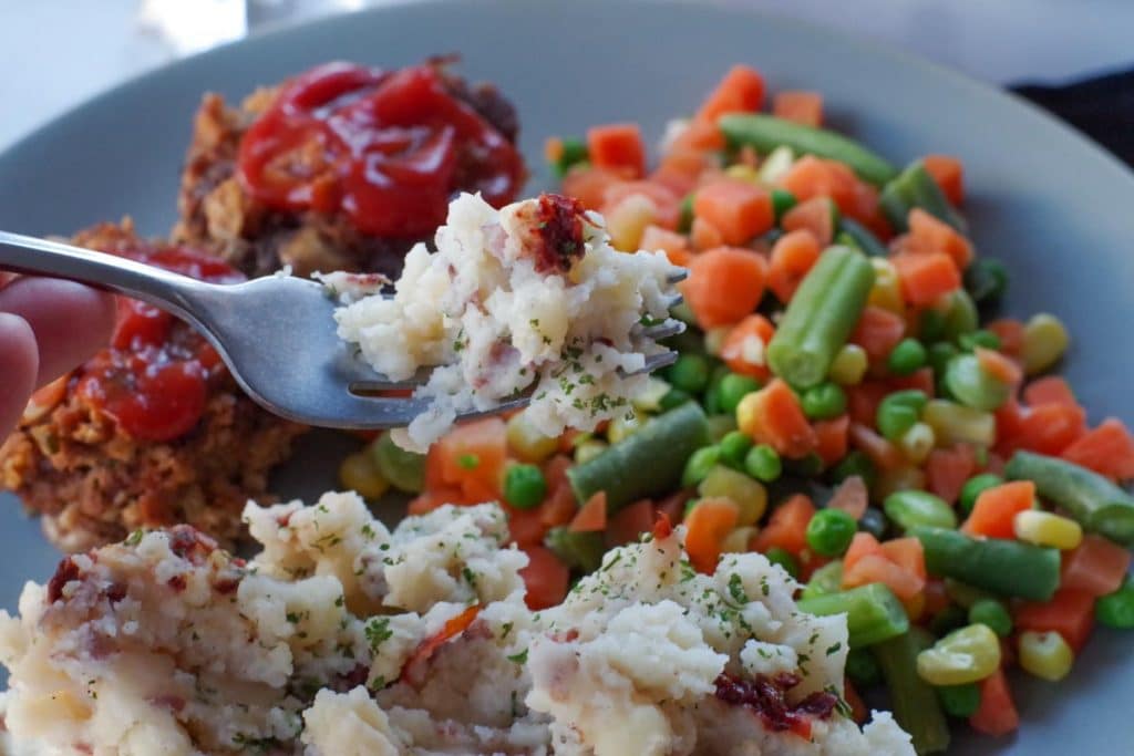 chipotle mashed potatoes being held up on a fork with meatloaf and vegetables on plate