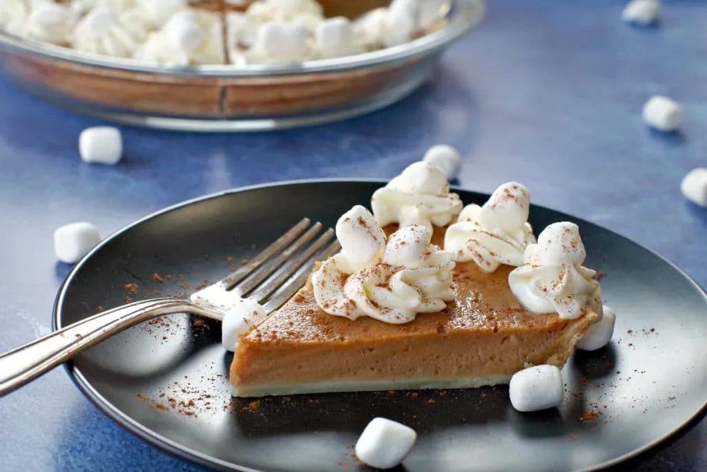 sweet potato pie on black plate on blue background with marshmallows around and pie in background
