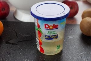 drained peach juice in dole peach container on black cutting board