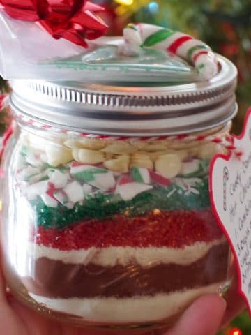 jar of homemade hot chocolate mix being held up in front of Christmas Tree