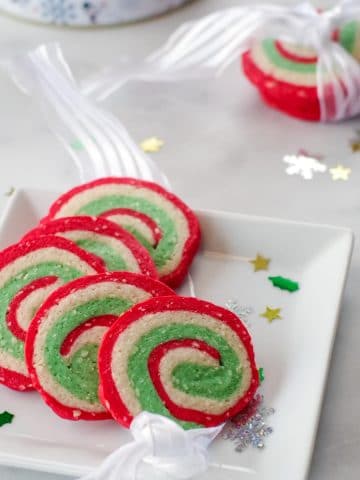 4 Christmas pinwheel cookies on a white plate with 3 cookies in a ribbon in the background