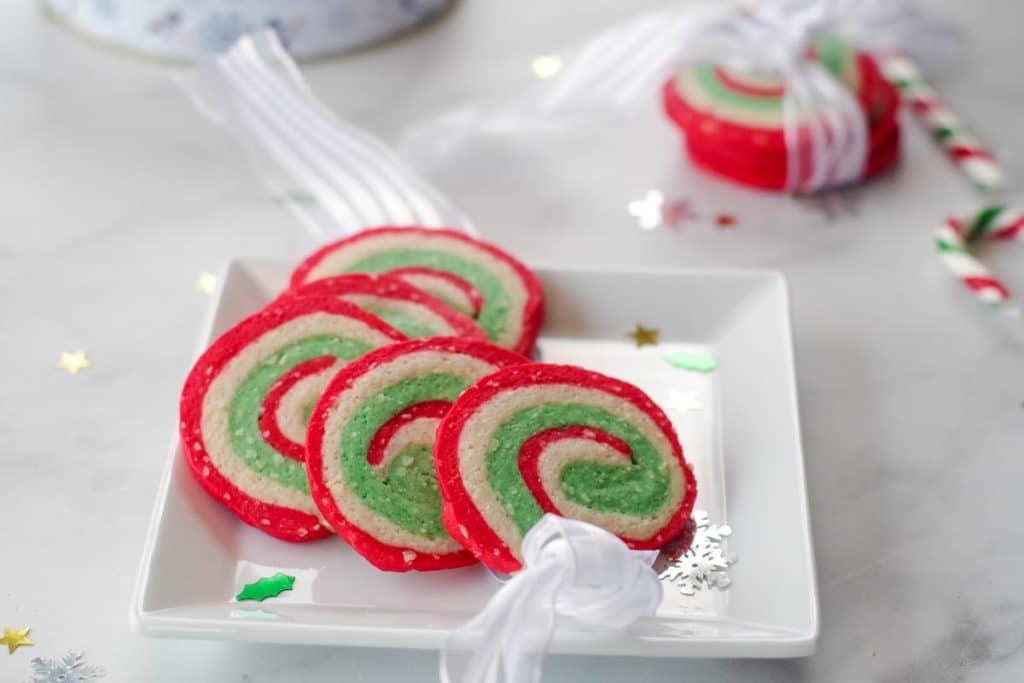 4 Christmas pinwheel cookies on a white plate with 3 cookies in a ribbon in the background
