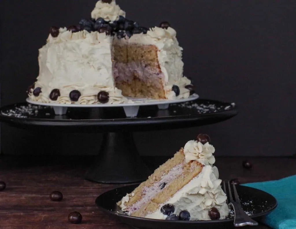 coffee layer cake on a black plate with layer cake on black platter in background