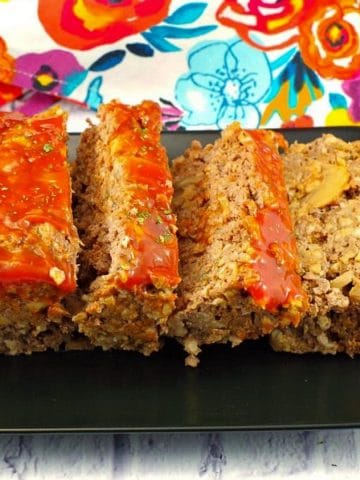 meatloaf, sliced on a black tray with a colorful flower tea towel in the background