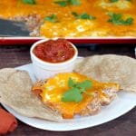 sheet pan huevos rancheros on a white plate with tortilla and salsa and sheet pan in background