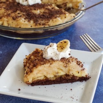 a piece of healthy banana cream pie on a white plate with a whole pie in the background