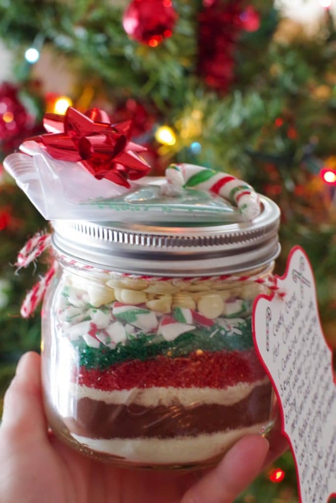 jar of homemade hot chocolate mix being held up in front of Christmas Tree