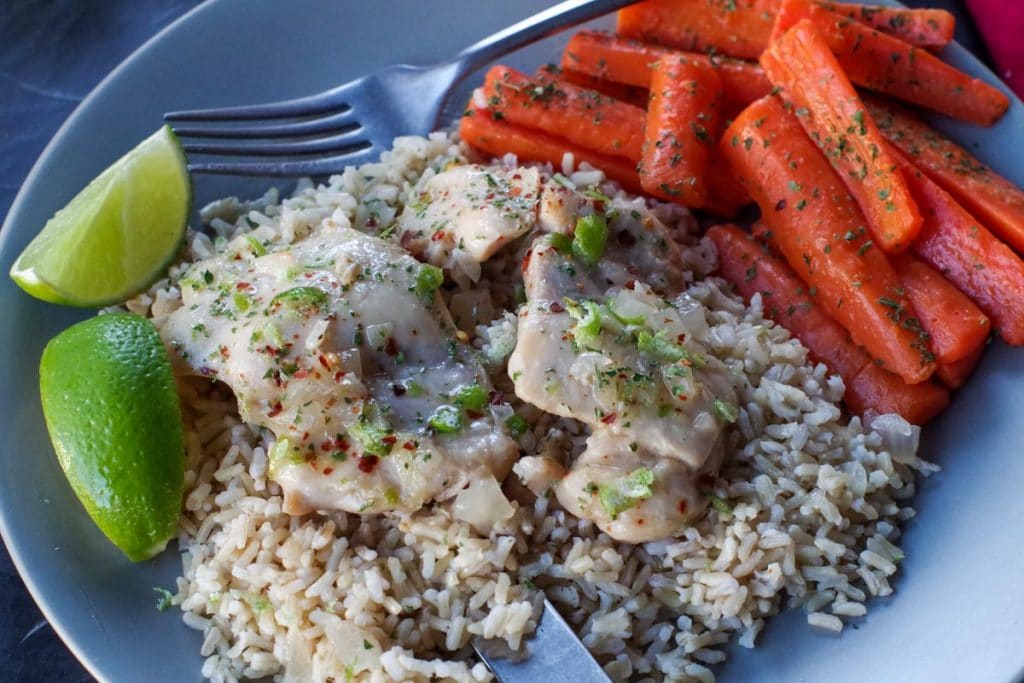 honey lime chicken over rice, with carrots on the side and lime wedges, on a grey plate