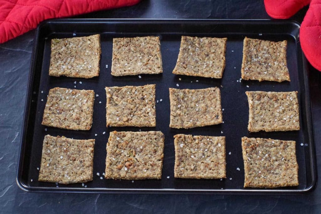 leftover stuffing crackers on a black baking sheet with red oven mitts in the background