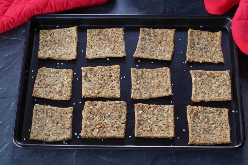 leftover stuffing crackers on a black baking sheet with red oven mitts in the background