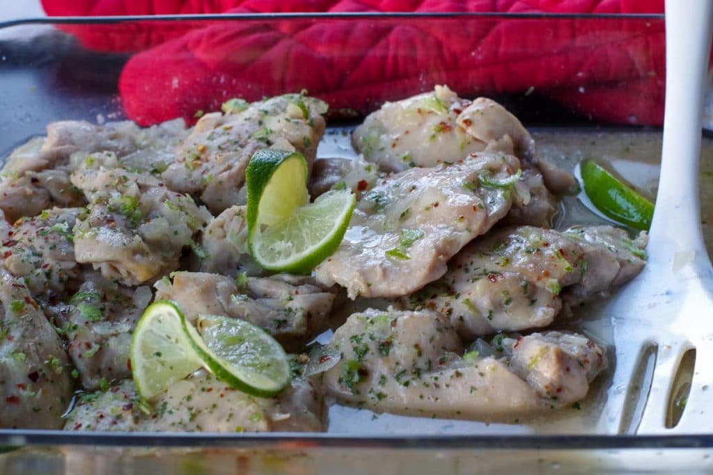 honey lime chicken thighs in a glass casserole dish with red oven mitts in the background