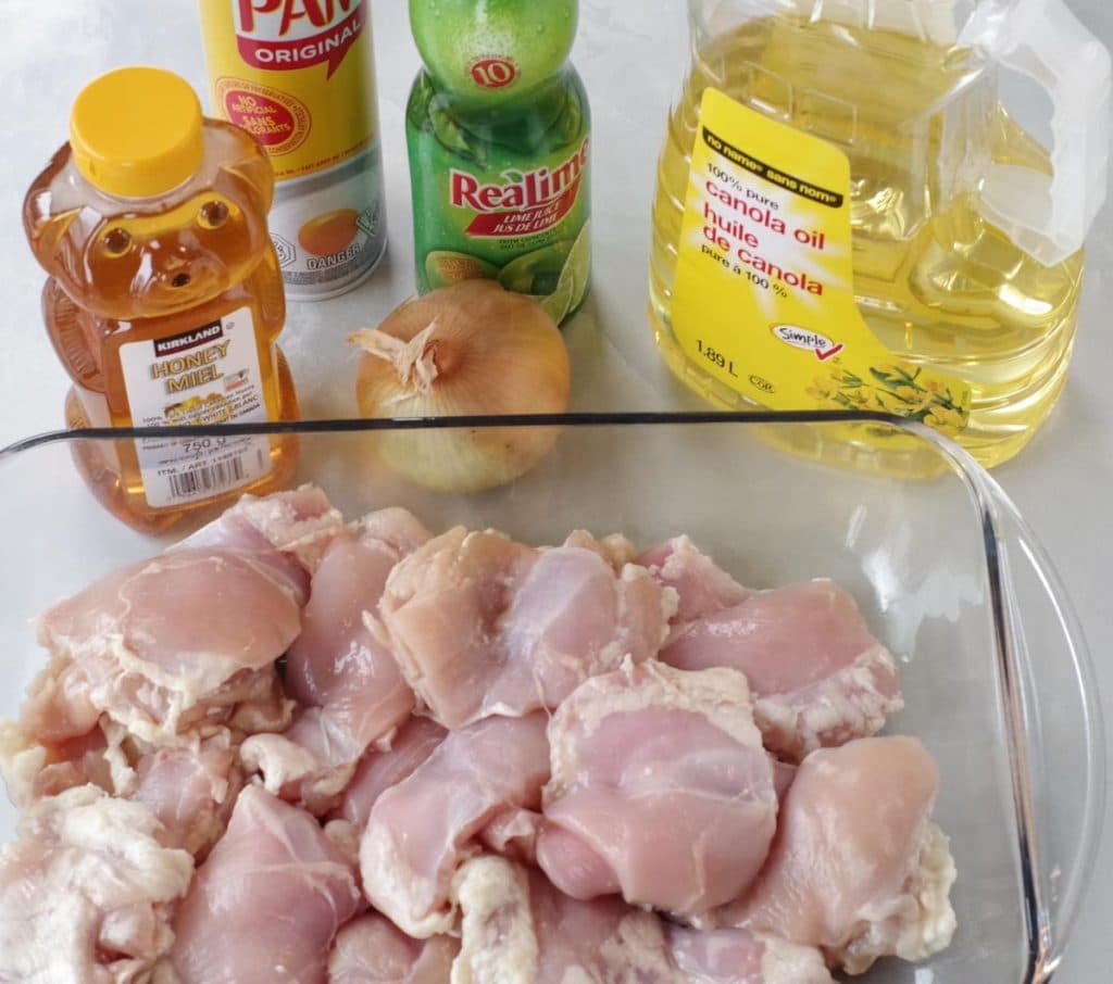ingredients (chicken thighs in casserole dish, lime juice, olive oil, honey, onion and pam spray) for honey lime chicken on a counter top