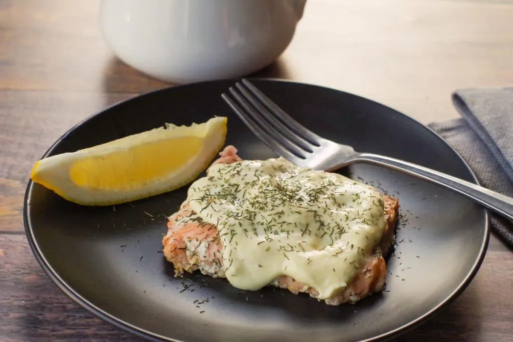 healthy and low-fat Hollandaise sauce on salmon, on a black plate, with fork and wedge of lemon