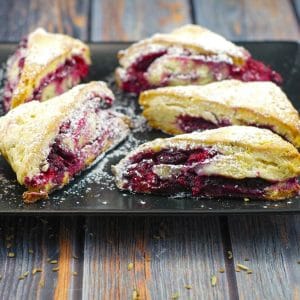 raspberry and lemon scones on a black platter on blueish faux wooden surface
