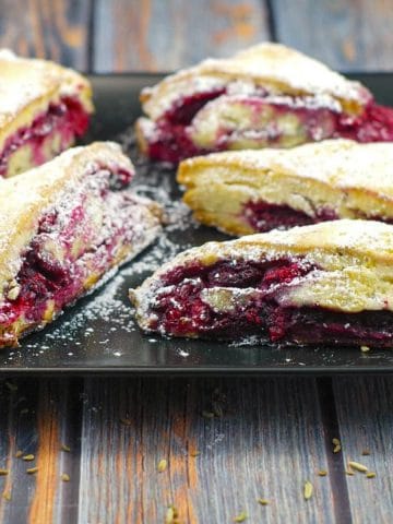 raspberry and lemon scones on a black platter on blueish faux wooden surface