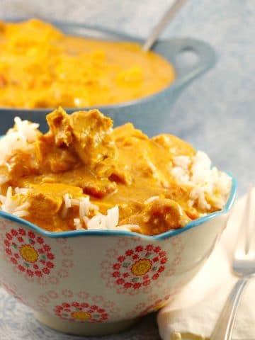 butter chicken in a patterned bowl with fork on the side and pot of healthy butter chicken in the background