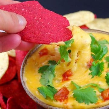 red tortilla chip being dipped into queso dip
