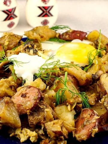 Ukrainian Breakfast Hash on a blue plate, with an egg on top and Ukrainian egg shaped shakers in the background