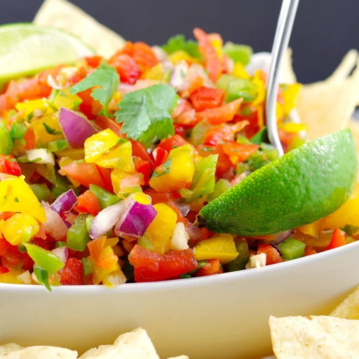 Pico de Gallo Salsa in a white bowl with a spoon, wedge of lime and tortilla chips on the side