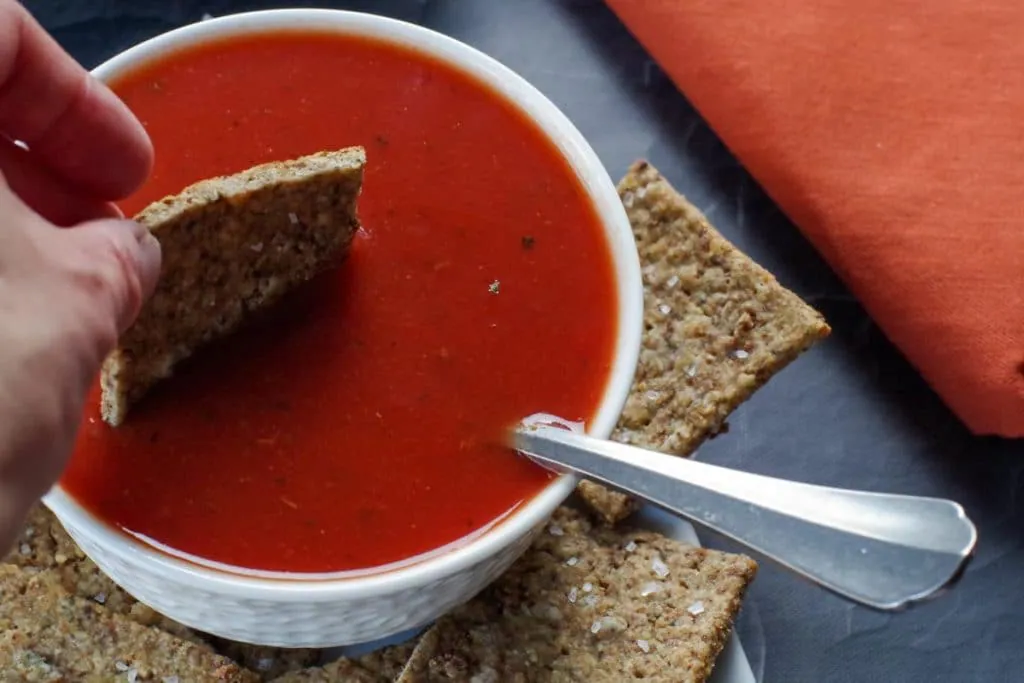 stuffing cracker being dipped into a bowl of tomato soup