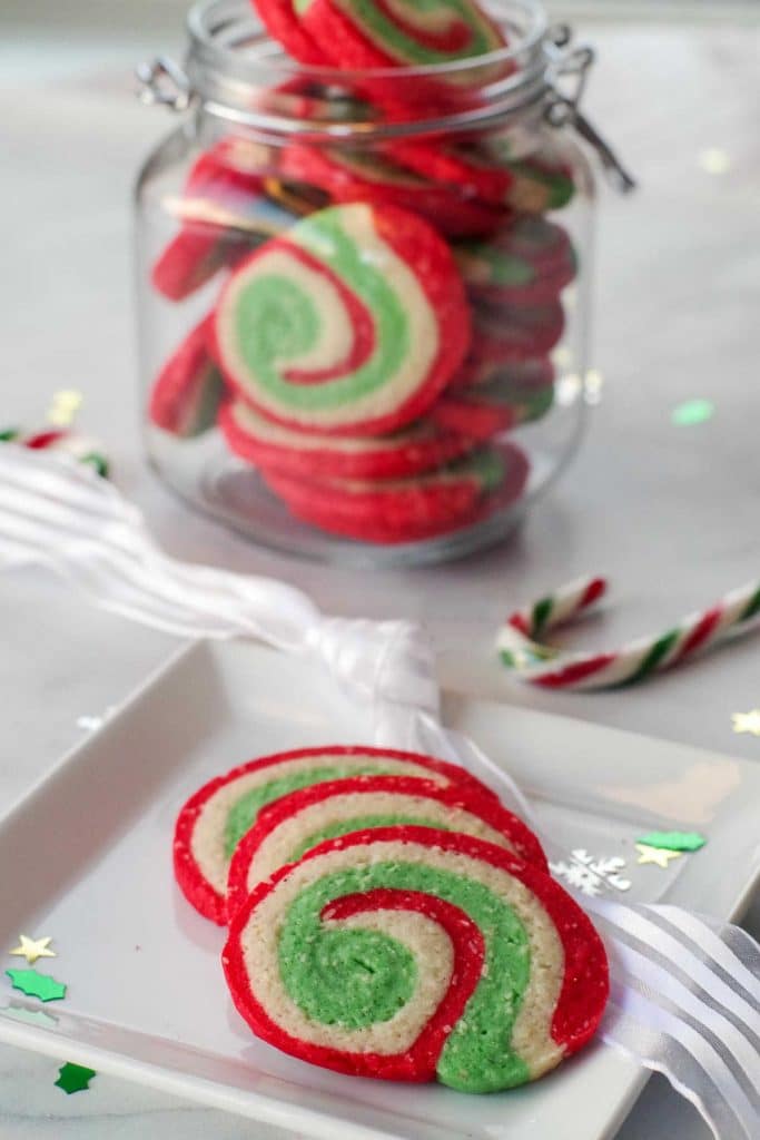 3 Christmas sugar swirl cookies on a plate with a jar of more cookies in the background