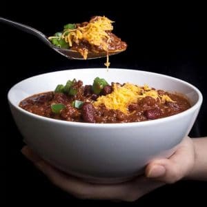 instant pot chili in a white bowl, with a spoon being held up over bowl