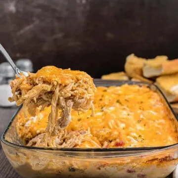 chicken spaghetti in a glass casserole dish with spoon holding up portion of it over the dish