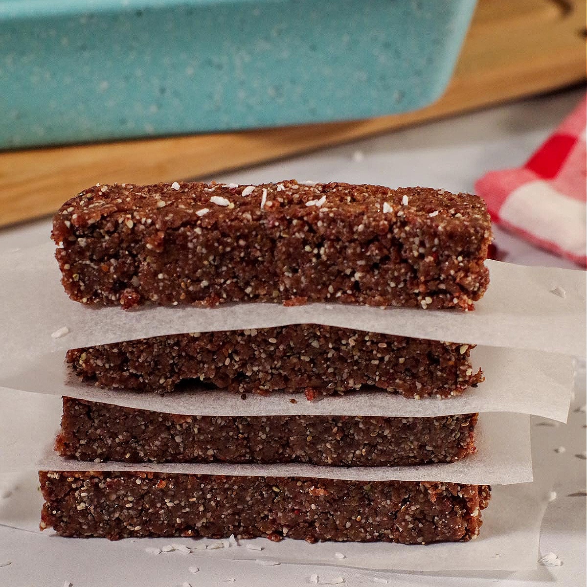 4 No bake energy bars stacked with parchment paper between them and blue loaf pan on cutting board in background