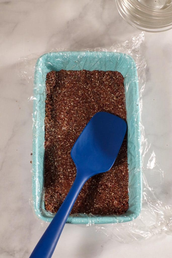 energy bars being pressed into blue loaf pan with blue spatula