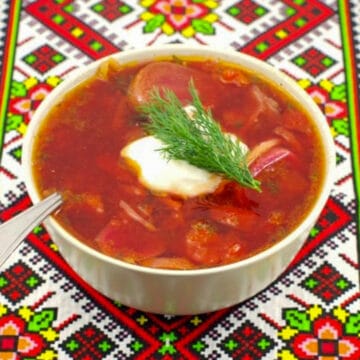 borscht soup in a beige bowl on a Ukrainian patterned tablecloth