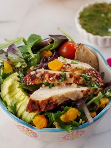 cajun chicken avocado mango salad in a bowl with small dish of dressing in the background