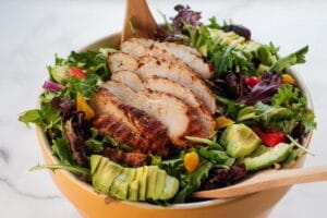 Cajun chicken avocado and mango salad in a large yellow bowl with serving untensils