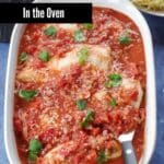 Chicken Cacciatore (in the oven) in a white casserole dish with a spoon in it.